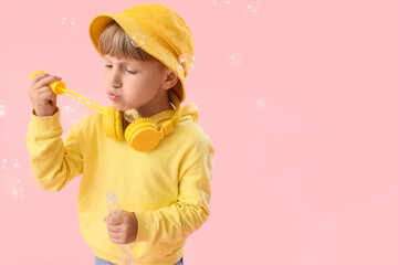 Cute little boy with headphones blowing soap bubbles on pink background