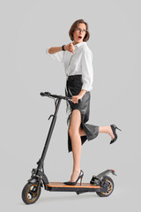 Surprised young businesswoman riding electric kick scooter on white background © Pixel-Shot