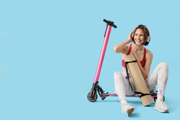 Sporty young woman in headphones with yoga mat and kick scooter on blue background