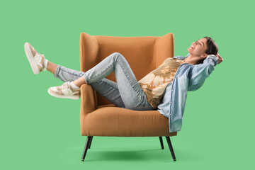 Happy young woman lying on armchair against green background