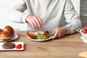 Man putting tomatoes on tasty burger in kitchen