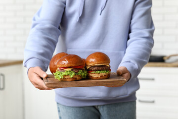 Man holding board with tasty burgers in kitchen