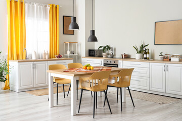 Interior of modern kitchen with white counters, dining table, yellow curtains, chairs and lamp