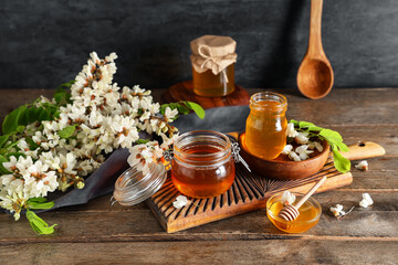 Jars and bowl of sweet honey with acacia flowers on wooden table