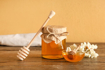 Bowl and jar of sweet honey with acacia flowers on wooden table