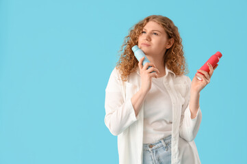 Thoughtful young woman with bottles of dry shampoo on blue background