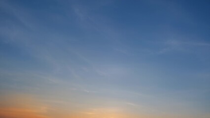 A tranquil sunset with a clear blue sky gently transitioning to warm hues of orange and yellow near...