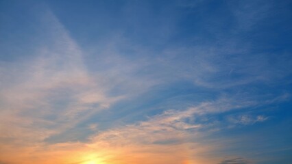 Obraz premium A beautiful sunset with the sun partially visible near the horizon. The sky transitions from warm oranges and yellows near the sun to cooler blues higher up. Sunset sky background. 