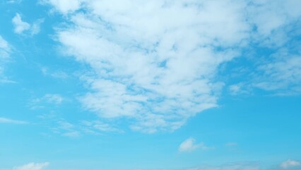 A clear blue sky adorned with fluffy white clouds scattered across the expanse. The light and airy...