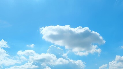 A clear blue sky with a few scattered, fluffy white clouds. The clouds are well-defined and float...
