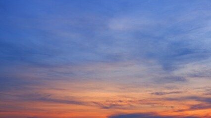 Obraz premium A serene sunrise with a sky transitioning from deep blue at the top to warm orange and pink tones near the horizon. The soft, wispy clouds add depth to the peaceful scene. Sunrise sky background.