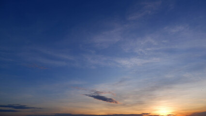 A tranquil sunrise with the sky gradually transitioning from deep blue at the top to soft oranges and yellows near the horizon. Wispy clouds are gently lit by the rising sun. Cloud background.
