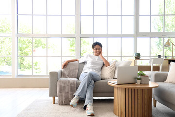 Young African-American woman sitting on grey couch at home