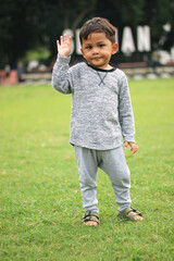 A handsome young boy, nicely dressed showing an expression of joy with hands up in the air looking excited and happy to be playing outdoors