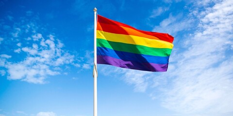 A rainbow flag waving in front of a clear blue sky in the background, representing pride month.
