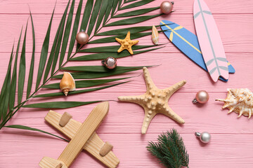 Wooden airplane, starfish, toy surfboard and palm branch with Christmas balls on pink wooden...