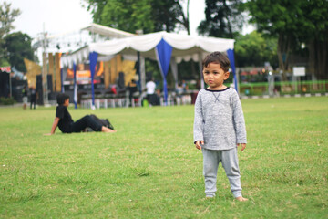 A handsome young boy, nicely dressed showing an expression of joy with hands up in the air looking excited and happy to be playing outdoors.
