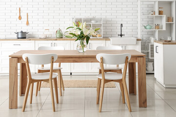 Vase with beautiful lily flowers on wooden dining table in kitchen