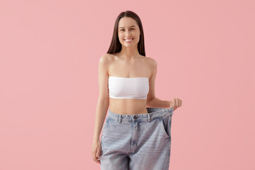 Beautiful young happy woman in loose jeans on pink background. Weight loss concept
