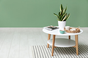 Coffee table with magazine, cup of tea and plant near green wall in room