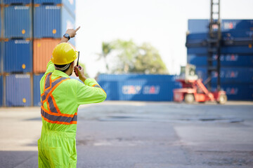 back view worker or engineer using walkie talkie and showing gesture to crane car in containers...
