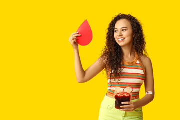 Young female African-American donor with applied medical patch, paper blood drop and pack for...