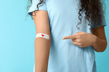 Young female African-American blood donor pointing at applied medical patch on blue background