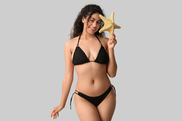 Beautiful young African-American woman in stylish black swimsuit with starfish on grey background