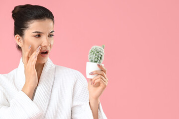 Beautiful young shocked woman with cactus on pink background. Depilation concept