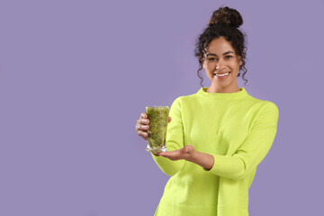 Beautiful young happy African-American woman with glass of tasty kiwi smoothie on purple background