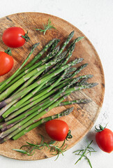 Fresh Asparagus and Tomatoes on a Wooden Cutting Board Against a White Background