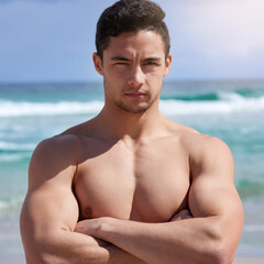 Arms crossed, muscles and portrait of man on beach in summer for holiday, travel or vacation. Sea, serious and sky with body of shirtless person on coast by ocean for exercise, fitness or workout