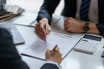 Close-up of business people discussing and signing a business contract, with documents and a calculator on the table.