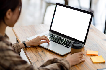 Woman working on a laptop at a wooden table, holding a coffee cup. Bright screen. Remote work,...