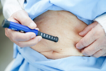 Asian senior woman making injection insulin pen in belly to treatment diabetes.