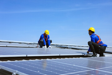 Two young caucasian workers are installing solar panels on the roof of industrial factory for renewable energy.