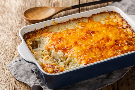 Сlassic Southern hashbrown casserole is made with sour cream, Cheddar cheese and condensed soup closeup in the baking dish on the wooden table. Horizontal