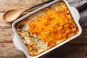 Homemade Cheesy Hashbrown Casserole with Potatoes and Cream closeup in the baking dish on the wooden table. Horizontal top view from above