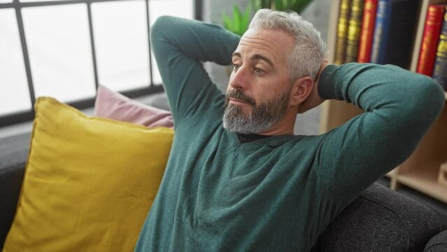 Relaxed middle-aged man with beard resting in a cozy living room on a sofa with colorful pillows