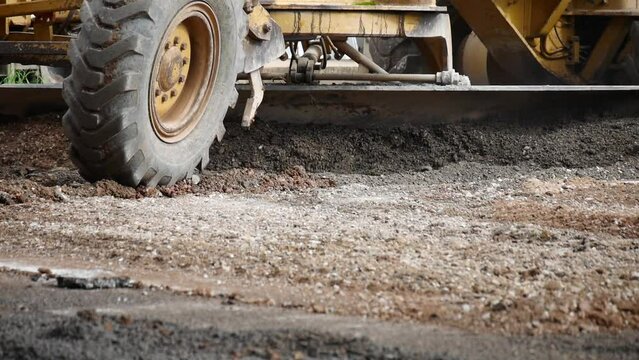 Grader Road Earthworks Construction, Grader working on gravel leveling, Road grader leveling gravel on road in rural landscape, Tracking shot of yellow road grader smoothing gravel surface for highway