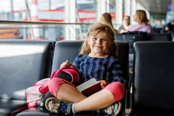 Little girl at the airport waiting for boarding at the big window. Cute kid holding...