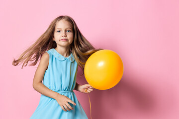 Joyful little girl in a blue dress holding a vibrant yellow balloon against a cheerful pink backdrop