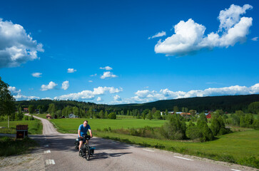 Cycling trip in Sweden, Cyclist on touring bicycle solo travel Nordic countryside, Road among fields summer day, Long distance cycling travel around the world, Mangskogsvägen south of Tobyn, Värmland