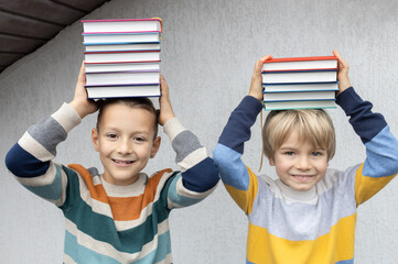 2 cheerful funny 8-year-old boys are holding a stack of books on their heads. back to school. Book Day. Read with pleasure. concept of reading, education, wisdom, knowledge. Digital detox