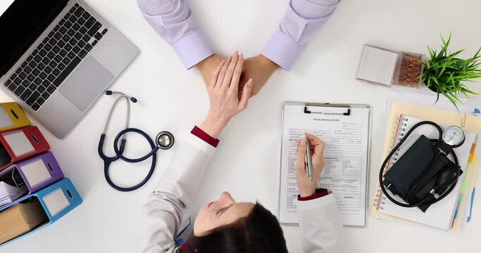 Friendly female doctor holding hand of patient sitting at table for encouragement and sympathy top view