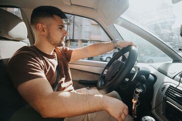 A focused young man drives his car through the city on a bright sunny day, demonstrating safe...