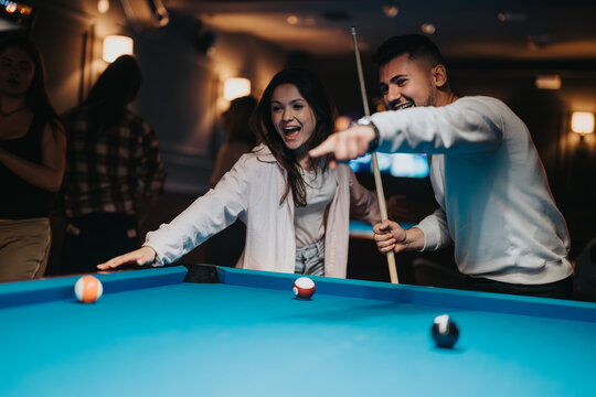 Excited young man and woman playing pool in a bar surrounded by friends, capturing a moment of joy and competition. - Powered by Adobe