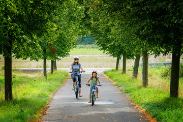Fototapeta premium Happy family is riding bikes outdoors and smiling. Mother and daughter, cute little preeschool girl on bicycles, active leisure and sports together.