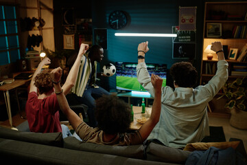Rear view of four young male friends enjoying watching soccer match on TV late in evening