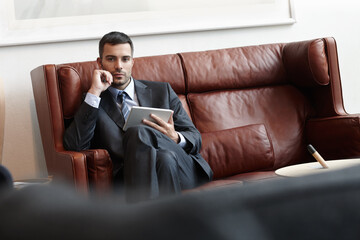 Businessman, serious and tablet on sofa in office or waiting room for appointment with lawyer in portrait. Worker, digital or professional on couch with tech for consult with browsing online in Spain